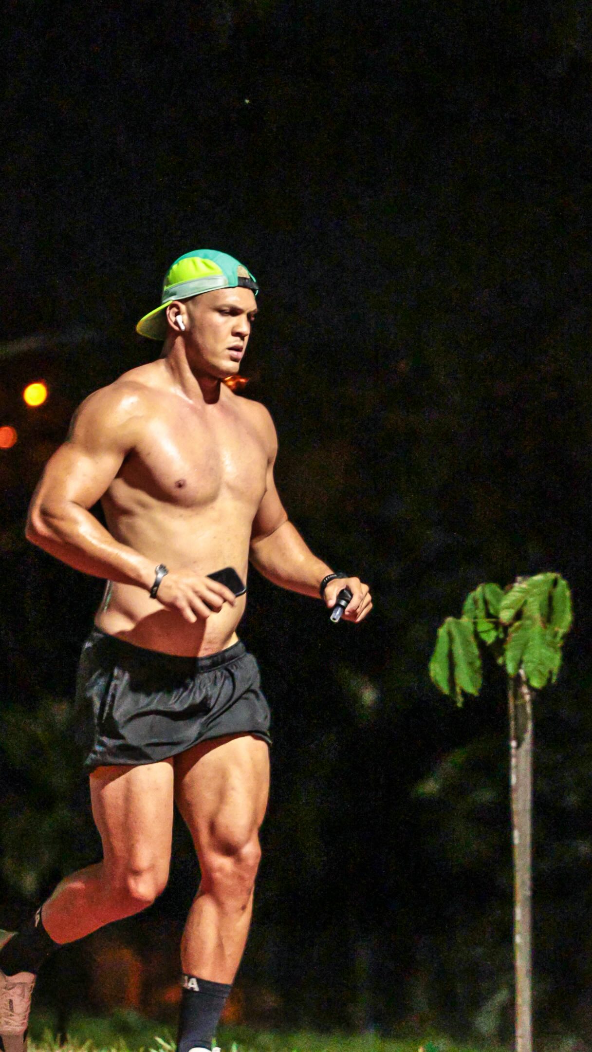 Matheus correndo à noite, sem camisa, de boné verde