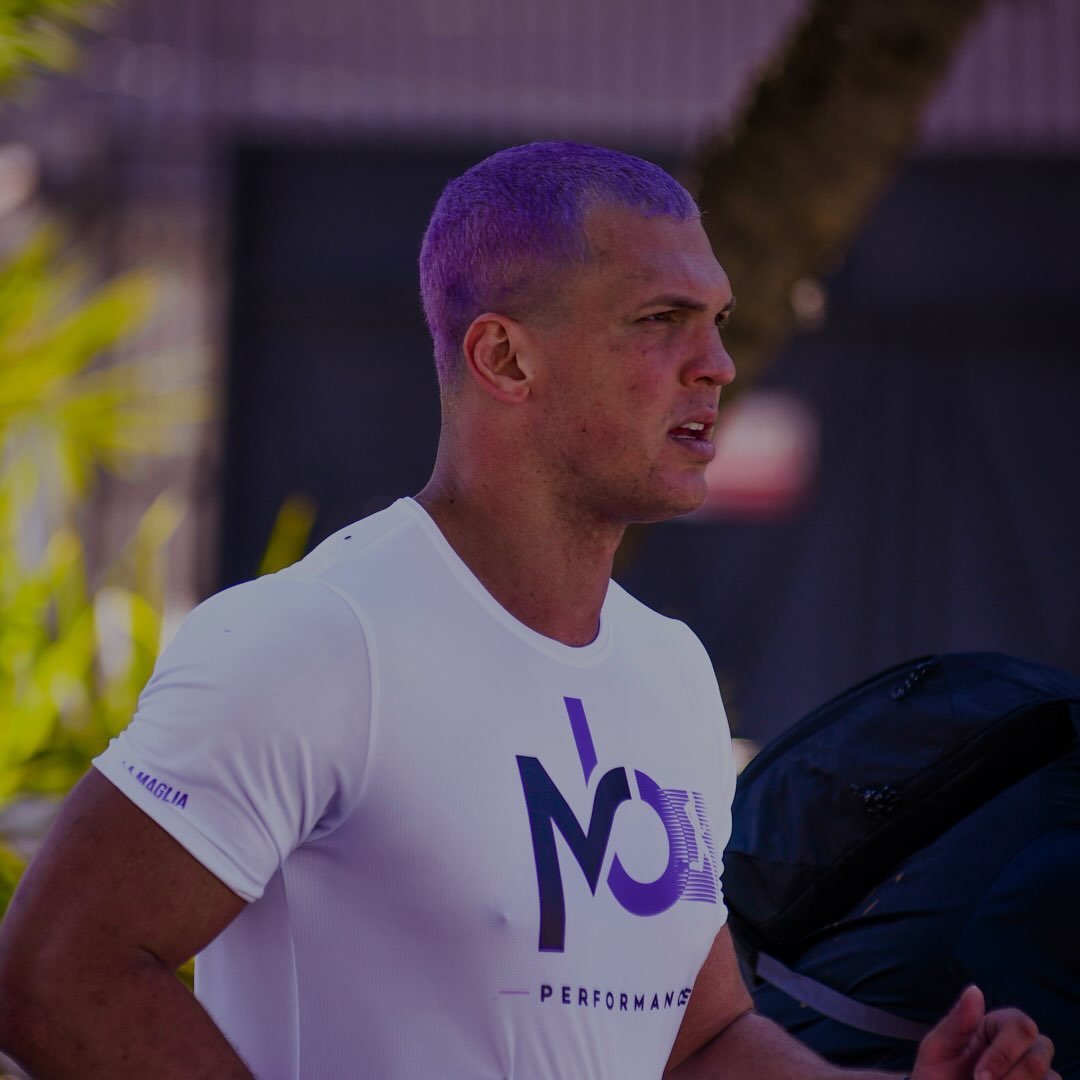 Retrato de perfil de Matheus Balsarini, cabelo pintado de roxo, camiseta branca MB Performance